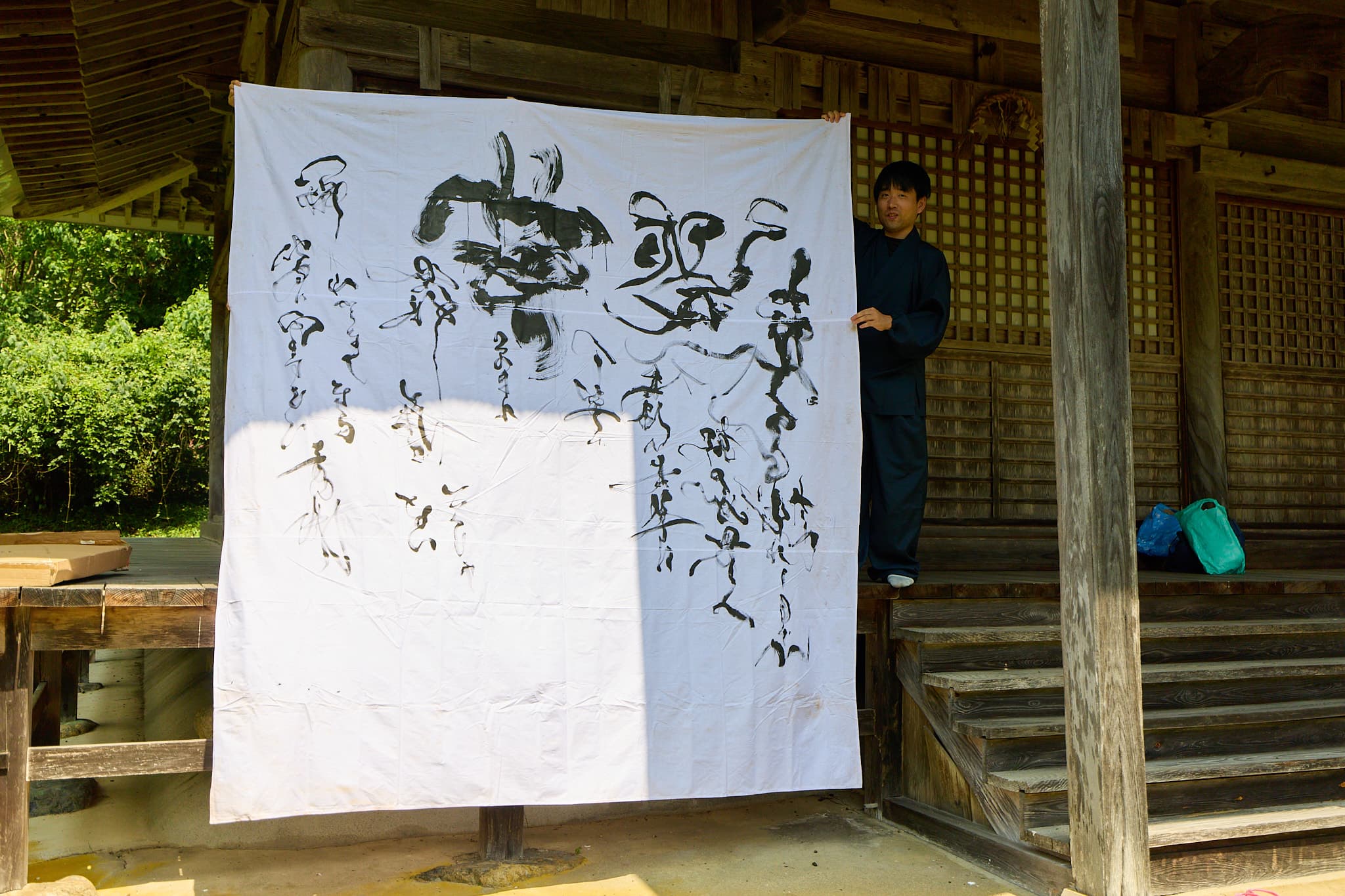 白布に草書で書き連ねた大型書道作品を、作務衣姿の森下友喜が掲げる様子