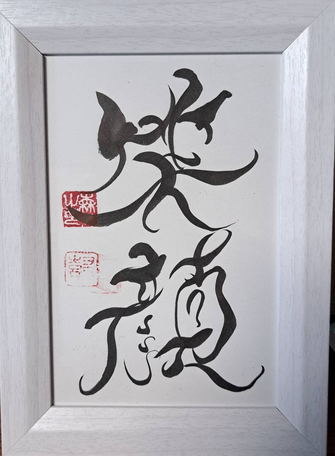 白木の額に収めた縦書きの二字「笑顔」。二顆の朱印を伴う