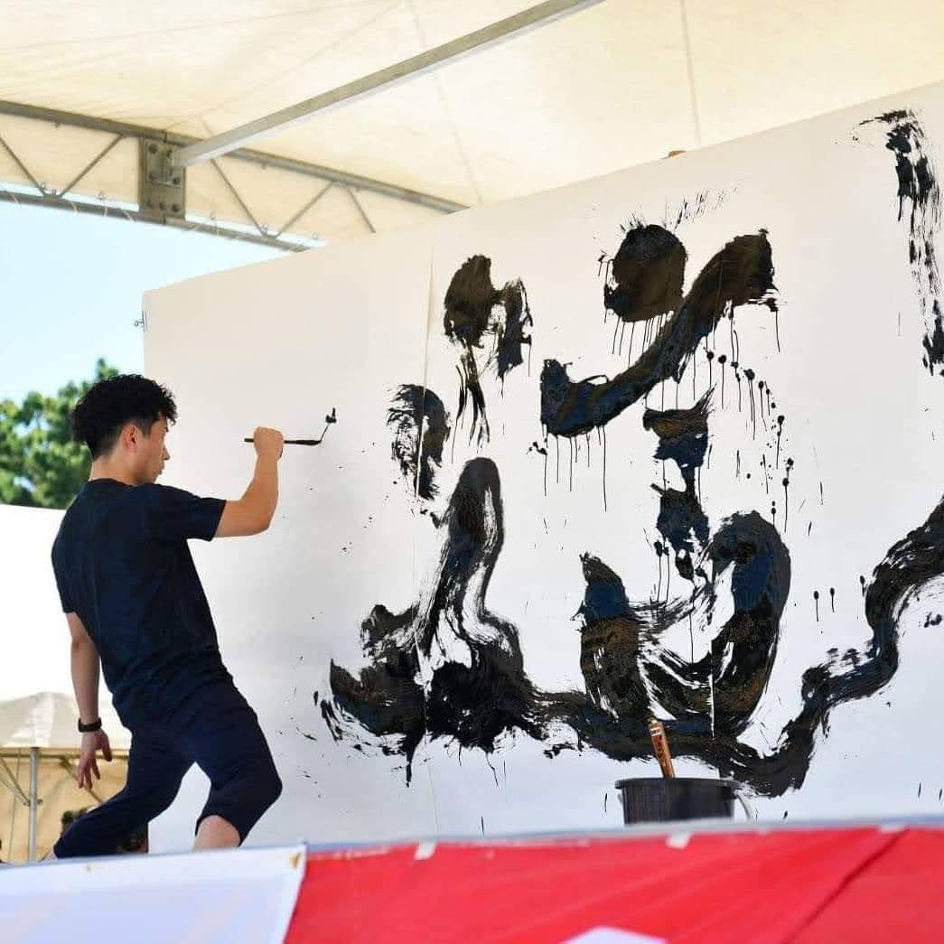 野外ステージで大判の紙に向かい、筆を走らせる作者